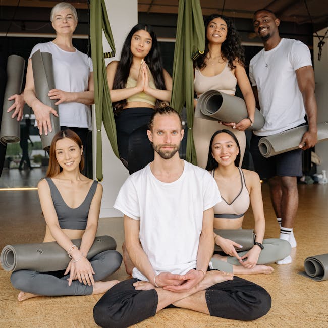 Group of people sitting in a lotus meditation pose in a bright studio.